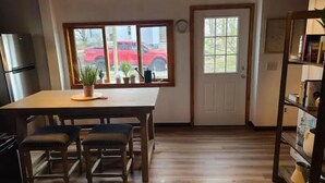 A kitchen with a wooden table, two chairs, a refrigerator, and a bookshelf. -  Carriage House in Old Saratoga (Schuylerville)