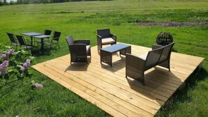 An outdoor seating area with wicker furniture on a wooden deck, surrounded by a grassy field and trees in the background. -  Carriage House in Old Saratoga (Schuylerville)