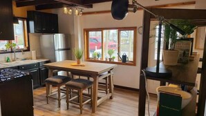 A kitchen with a wooden table, stools, a stove, and a window with plants. -  Carriage House in Old Saratoga (Schuylerville)