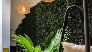 Una silla colgante con cojín, una lámpara colgante y una pared cubierta de follaje verde.