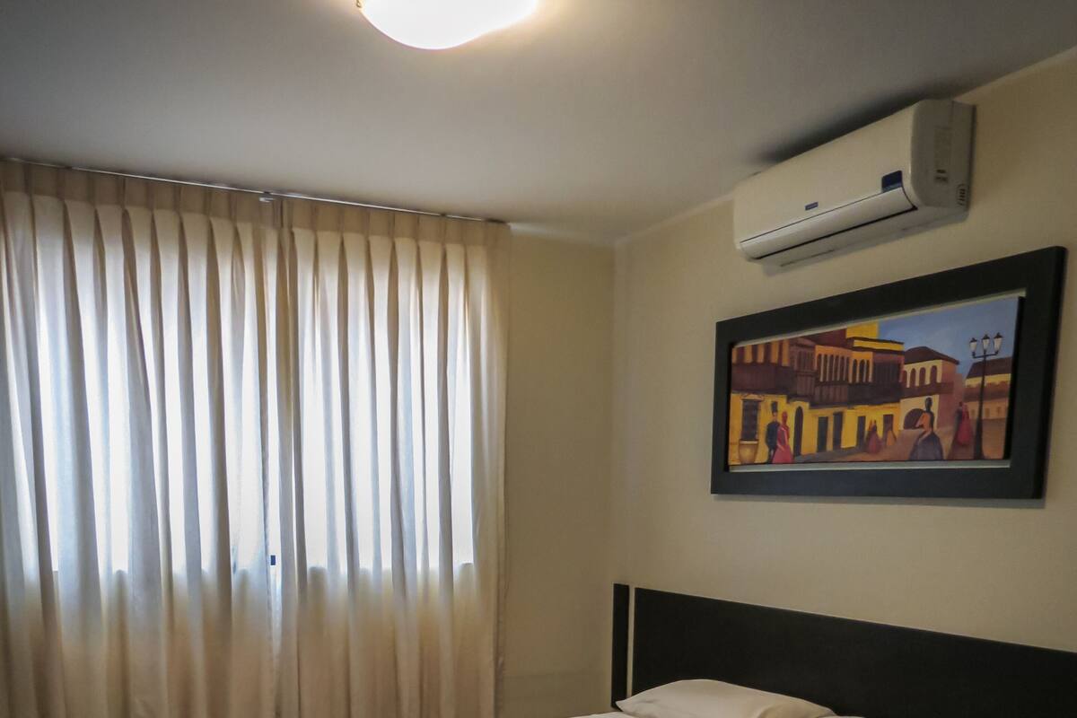Ein Hotelzimmer mit Bett, Vorhängen, einer Klimaanlage und einem Gemälde an der Wand.