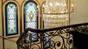 Una imponente escalera con barandales de hierro ornamentados, un gran candelabro de cristal y dos ventanas con vidrieras de intrincados diseños.