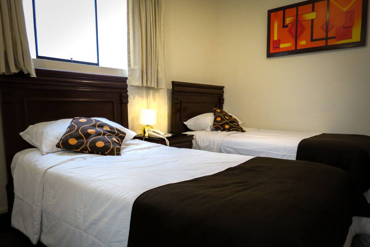 Zwei Einzelbetten mit weißen Laken und braunen Kopfteilen in einem Hotelzimmer.