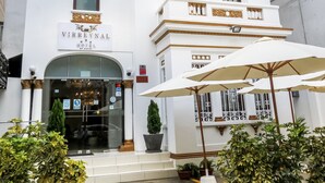 Un edificio blanco con un letrero que dice "VIRREYNAL HOTEL". Hay escalones que conducen a la entrada y sombrillas exteriores dispuestas al frente.