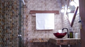 Un baño con cabina de ducha de vidrio, lavamanos rojo y espejo con iluminación.