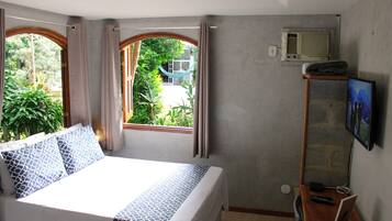 Un dormitorio con cama, escritorio, televisión y ventana con cortinas.