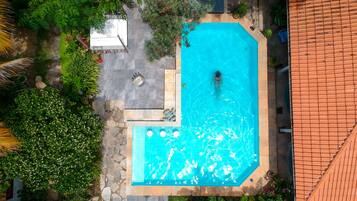 Une vue aérienne d’une piscine entourée d’une végétation luxuriante et de sentiers en pierre.