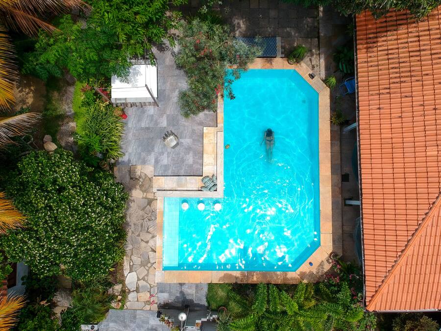 Une vue aérienne d’une piscine entourée d’une végétation luxuriante et de sentiers en pierre.