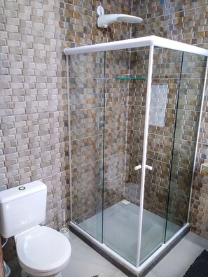 A shower enclosure with glass doors, a toilet, and a tiled wall. - Jardim Secreto Guest House - Hostel (Búzios)
