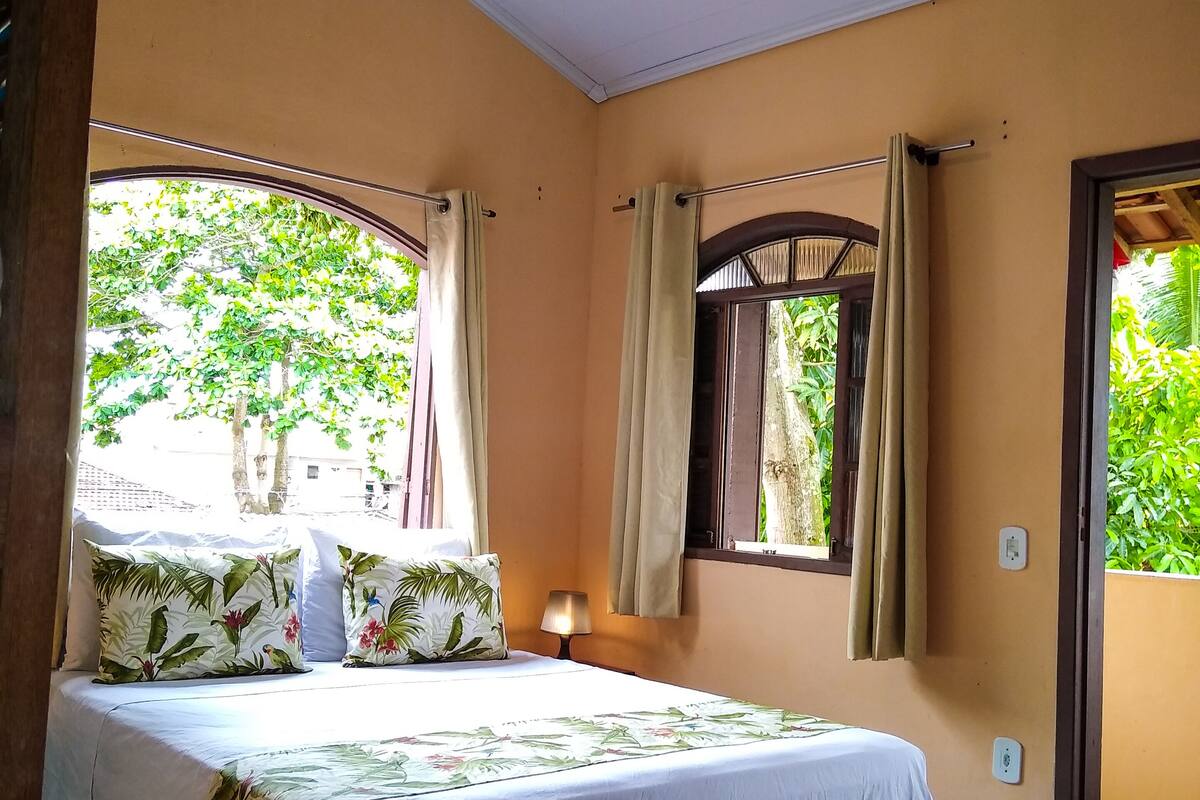 A bedroom with a bed, a ceiling fan, a window with curtains, and a view of greenery outside.