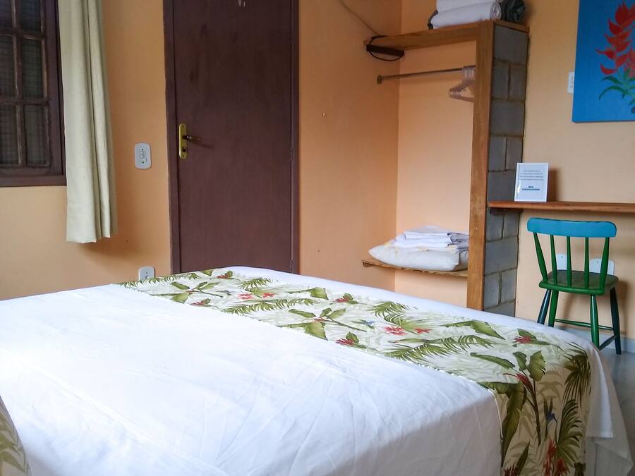 A hotel room with a bed, a desk, a chair, an air conditioner, and a door.