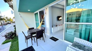 A modern outdoor seating area with a table and chairs, a hammock, and a glass door leading to a room. - Villas Do Atlântico (Ipojuca)