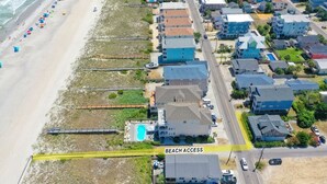 Vue aérienne d’une zone résidentielle côtière, avec des maisons, une plage et un sentier balisé indiquant l’accès à la plage.