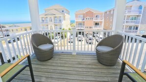 Un balcon avec deux fauteuils en osier et une vue sur des immeubles à plusieurs étages et des voitures garées.