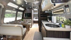 A compact RV interior with a kitchenette, dining area, and a small sleeping space.