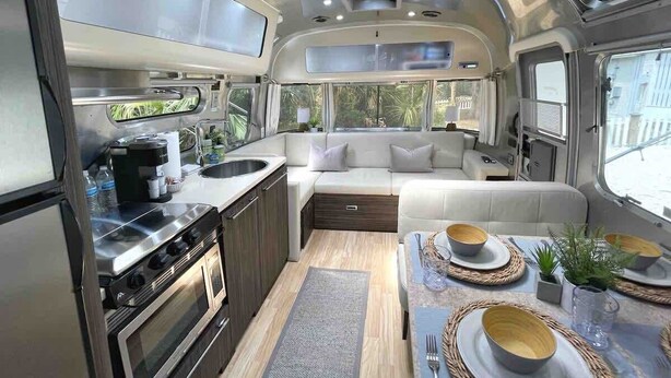 A compact RV interior with a kitchenette, a dining area, and a seating area with a view of the outdoors.