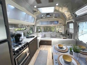 A compact RV interior with a kitchenette, a dining area, and a seating area with a view of the outdoors.