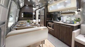 A compact RV interior with a kitchenette, a dining area, and a seating space.