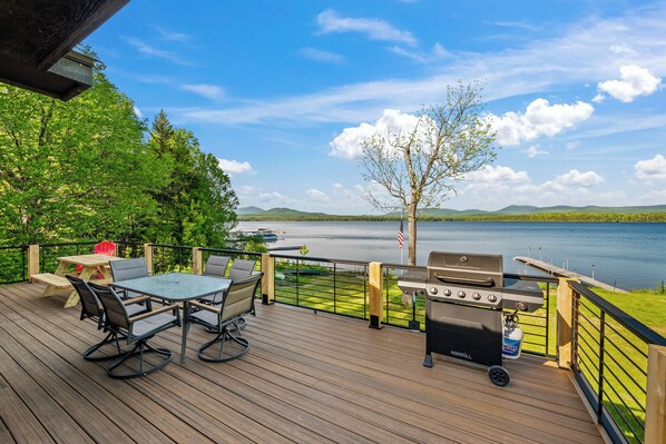 A deck with a table and chairs, a grill, and a view of a lake.