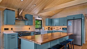 Une cuisine moderne avec des poutres en bois au plafond, un îlot central doté de tabourets et des appareils électroménagers en acier inoxydable.