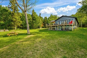 A modern cabin with a deck, surrounded by a grassy area and trees.