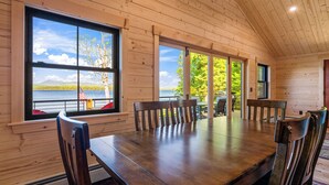 L’intérieur d’un chalet en bois comprend une grande table à manger, plusieurs chaises et de grandes fenêtres offrant une vue panoramique.