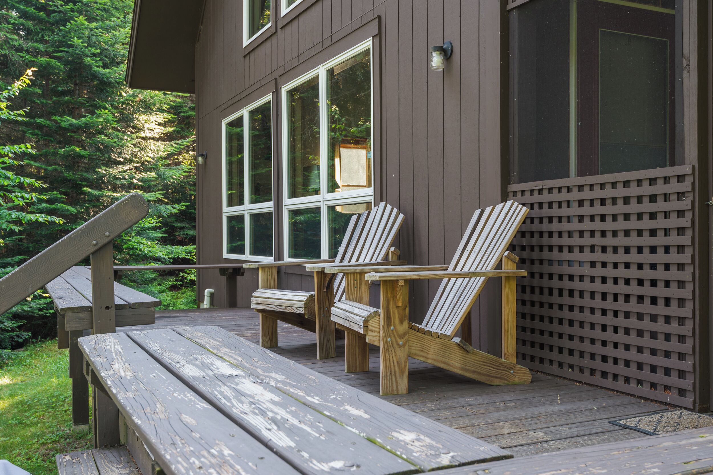 A wooden deck with two Adirondack chairs and a bench.