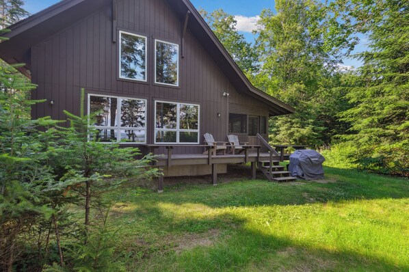 Ein zweistöckiges Holzhaus mit Terrasse, großen Fenstern und einer überdachten Grillgelegenheit.