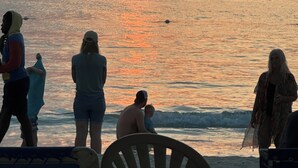 Un atardecer sobre el océano con gente en la playa.
