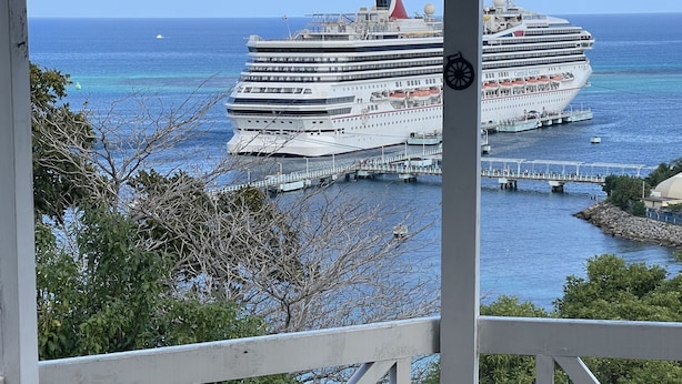 Vista de un crucero amarrado en un puerto, con cielo azul despejado y el océano al fondo.