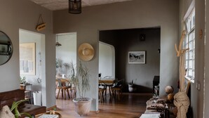 Amplia sala de estar con piso de madera, una maceta tejida grande, una mesa de comedor con sillas y una zona de estar acogedora con un sofá y una mesa redonda pequeña.