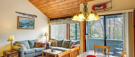A cozy living room with a wooden ceiling, a sofa, a coffee table, and a dining area with chairs.