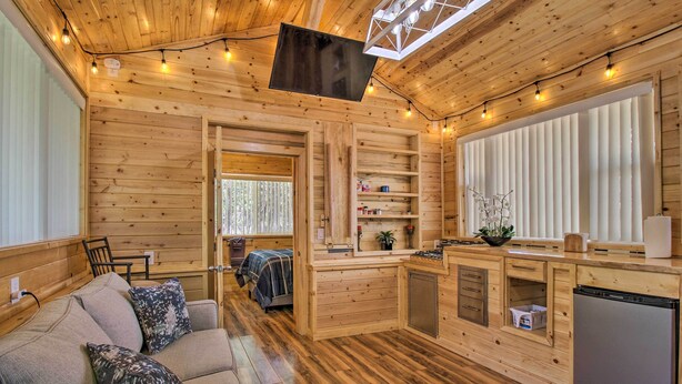 A cozy cabin with a wooden interior, a sofa, a TV, and a kitchen area. - Grill, Fire Pit: Pet-Friendly Lakeside Cottage! (Lakeside)