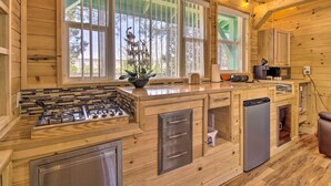 A wooden cabin kitchen with a gas stove, refrigerator, and a window with a view of trees. - Grill, Fire Pit: Pet-Friendly Lakeside Cottage! (Lakeside)