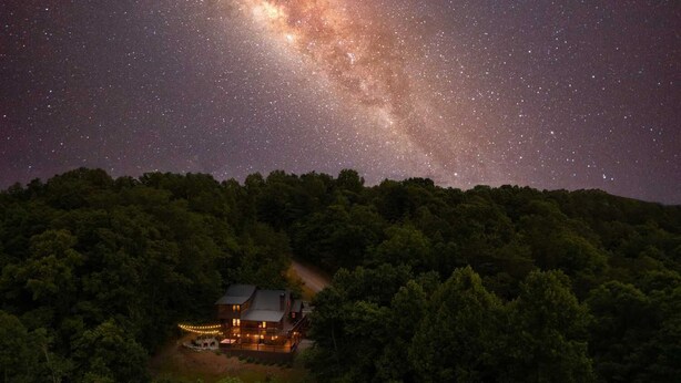 A cabin surrounded by dense forest with a starry night sky above. - Mountain View Cabin - Hot Tub - Fire Pit - Pool Table - Game Room (Mineral Bluff)