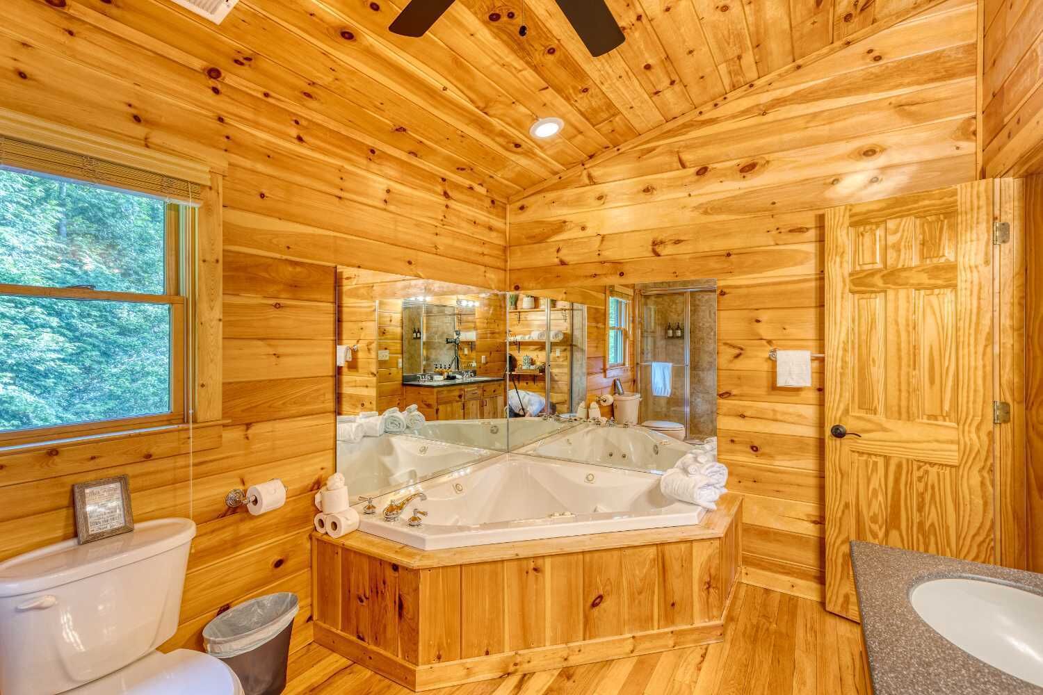 A wooden cabin bathroom with a large bathtub, a toilet, and a shower area.