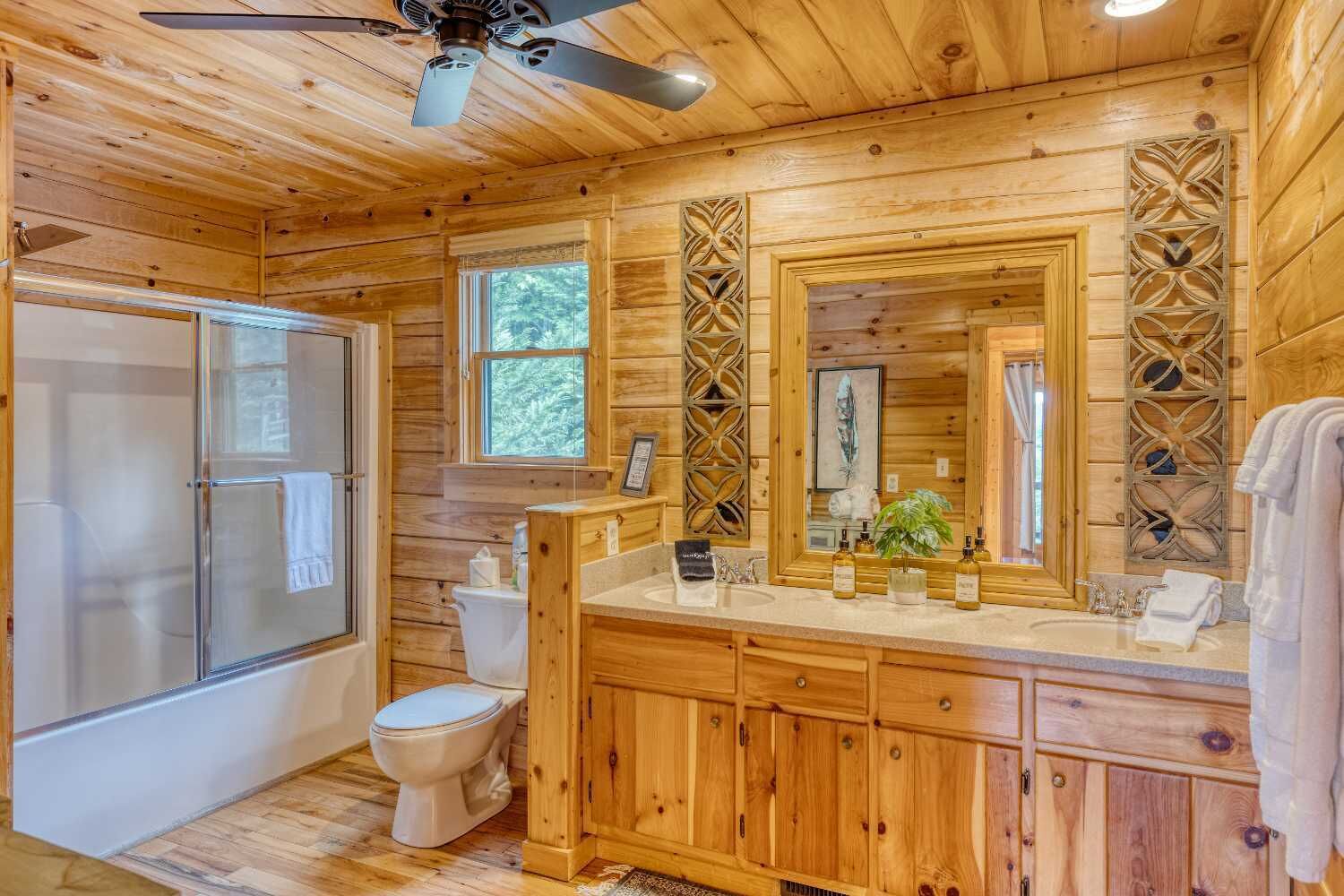 A wooden cabin bathroom with a shower, toilet, vanity, and a ceiling fan.