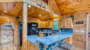 A wooden cabin with a kitchen featuring a stone island, wooden cabinets, and a view of the outdoors. - Mountain View Cabin - Hot Tub - Fire Pit - Pool Table - Game Room (Mineral Bluff)