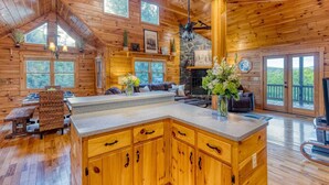 A spacious cabin with a large wooden interior, a stone fireplace, and a balcony with a view of the surrounding forest. - Mountain View Cabin - Hot Tub - Fire Pit - Pool Table - Game Room (Mineral Bluff)