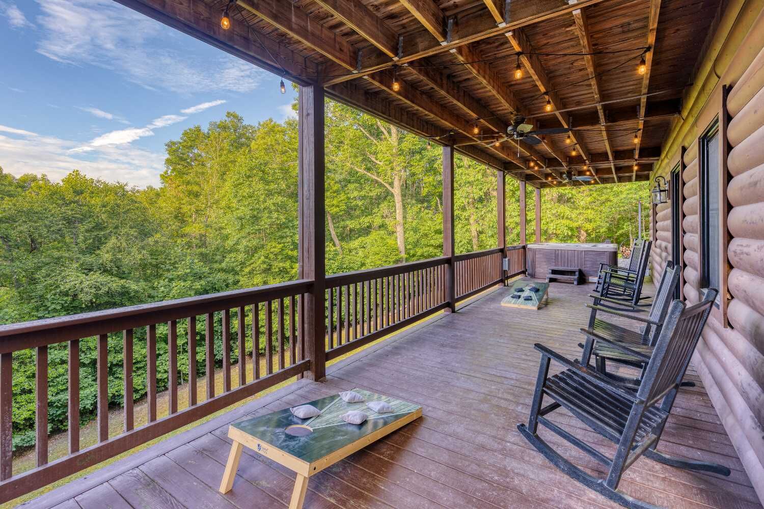 A covered porch with a view of a forest, wooden deck, and outdoor seating area.
