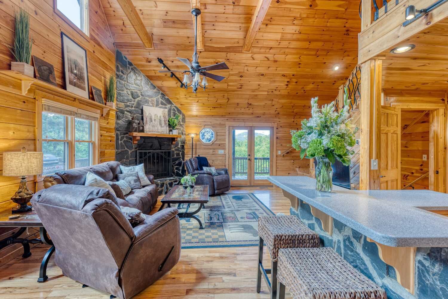 Un intérieur chaleureux de chalet en bois, avec une cheminée en pierre, des canapés en cuir et un mur d’accent en pierre.