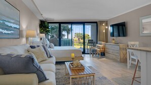 Ein modernes Hotelzimmer mit Bett, Sofa, Schreibtisch und Blick auf Palmen sowie ein Gebäude.