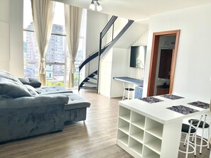 Un salon moderne avec un canapé gris, une table basse blanche et un escalier menant à un balcon.