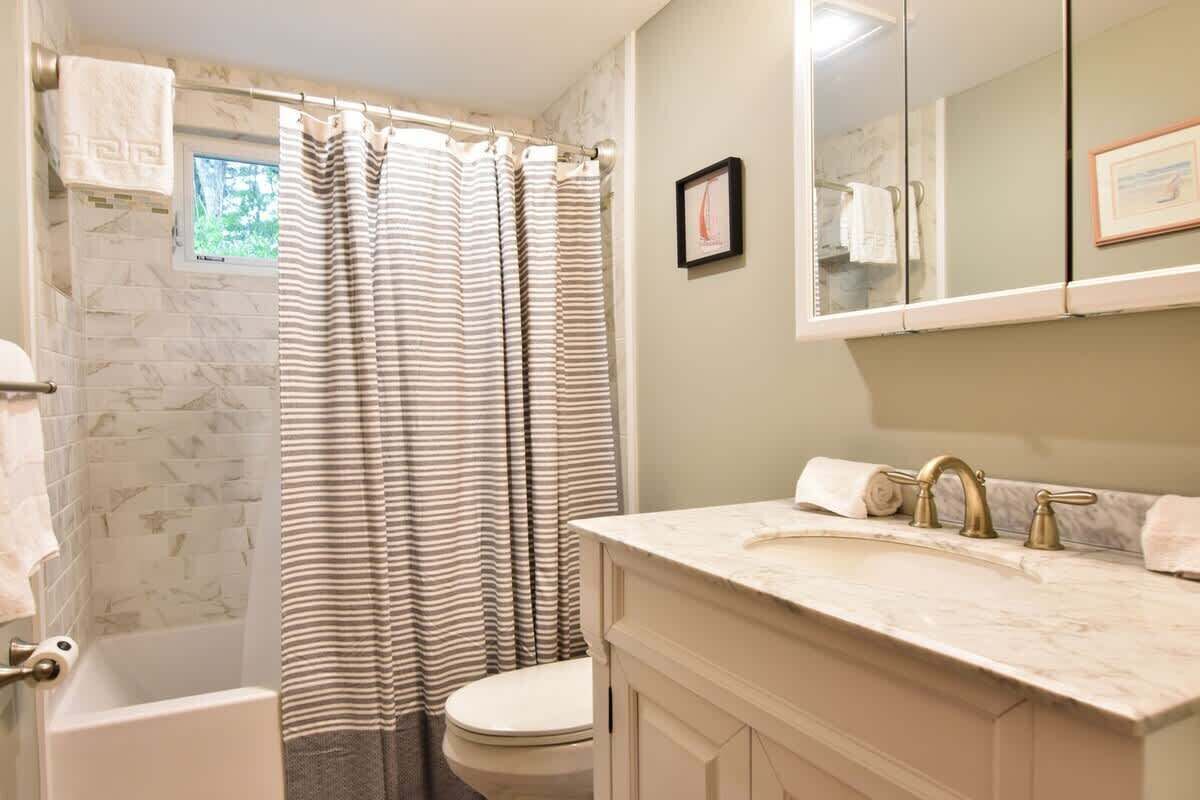 Un baño con bañera, inodoro y tocador con lavabo y espejo.