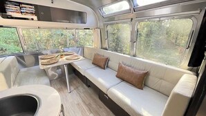 A compact, modern RV interior with a sofa, a small table, and a built-in sink. - Chic Airstream Glamper Near Tybee & Savannah (Savannah)