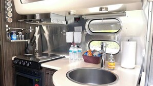 A compact kitchenette with a stove, oven, sink, and small window. - Chic Airstream Glamper Near Tybee & Savannah (Savannah)