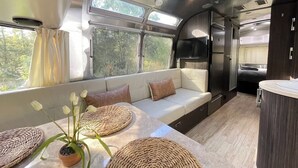 A compact RV interior with a sofa, a small kitchen area, and a dining space with woven placemats. - Chic Airstream Glamper Near Tybee & Savannah (Savannah)