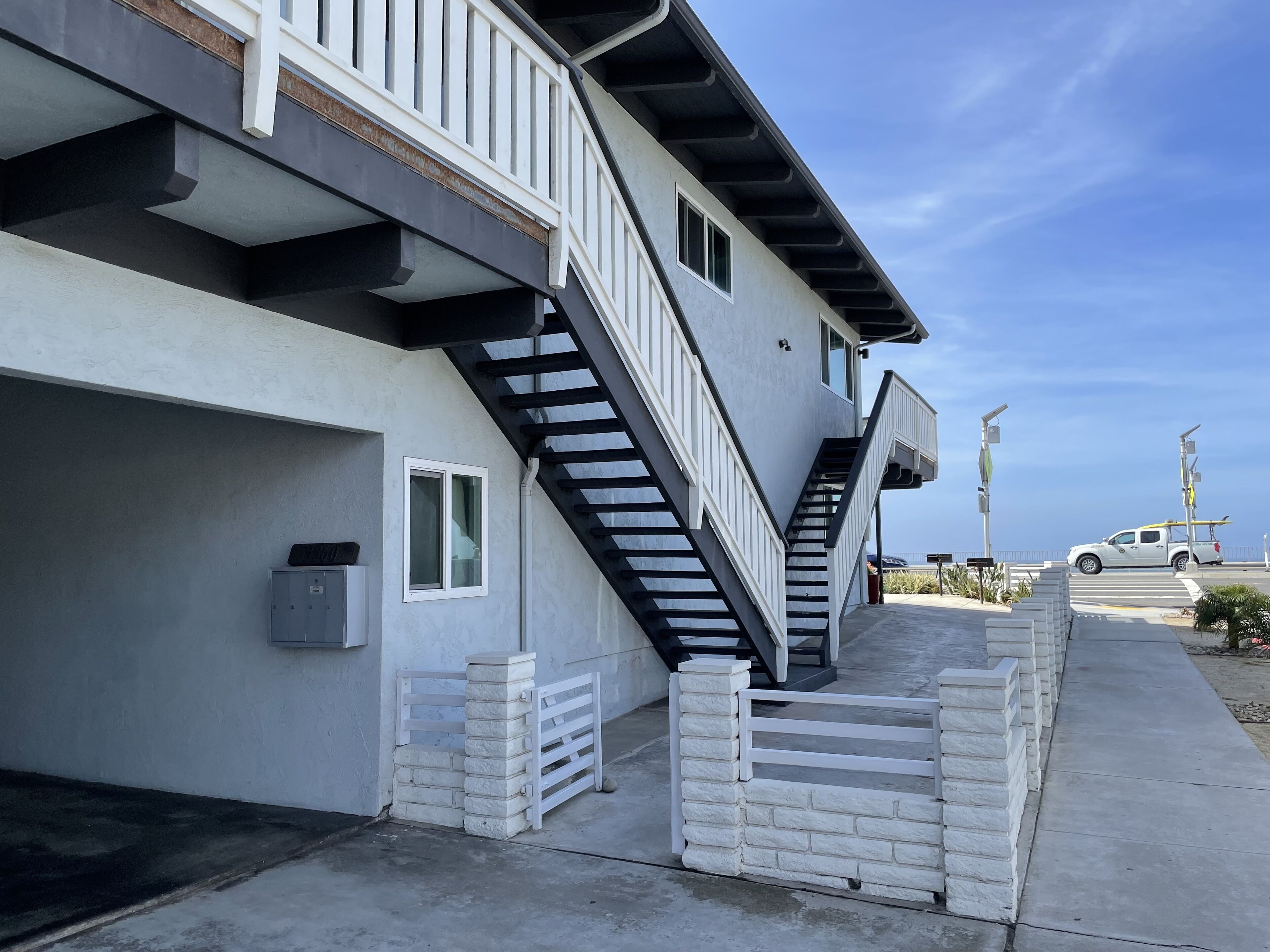A two-story building with a black exterior, white railings, and a concrete staircase leading to the upper floor.