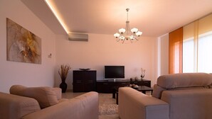 A modern living room with a flat-screen TV, a chandelier, and beige sofas. - Holiday apartment mit Pool und Klimaanlage (Mekiši kod Vižinade)