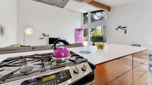 A modern kitchen with a gas stove, wooden cabinets, and a large window. - Plum Perfect | Cozy SoCo Stay + Yard & Style (Austin)